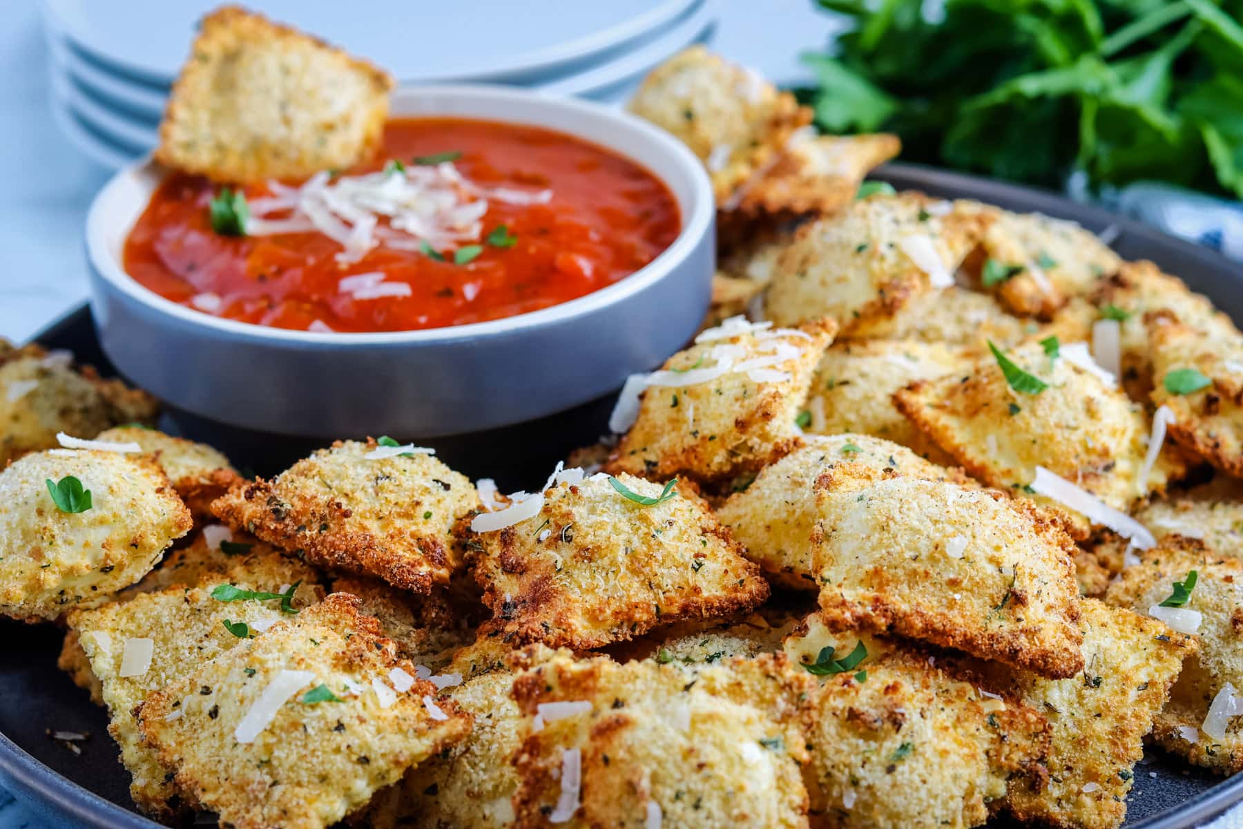 Crispy air fryer ravioli on a plate with one dipping into a sauce.