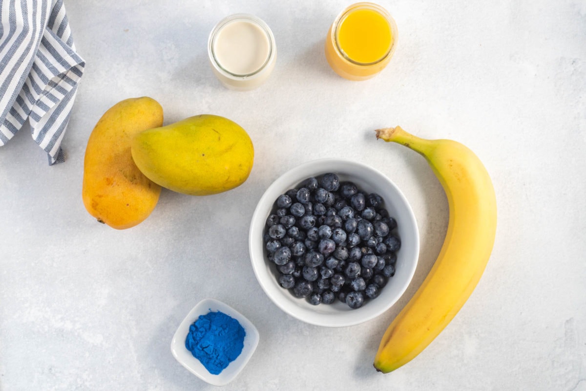 ingredients for the blueberry mango smoothie - banana, mango, blueberries, orange juice, coconut milk and blue spirulina powder