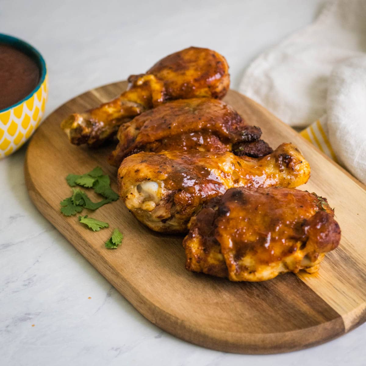 Chicken drumsticks and thighs coated with BBQ sauce on a wooden cutting board with herbs.