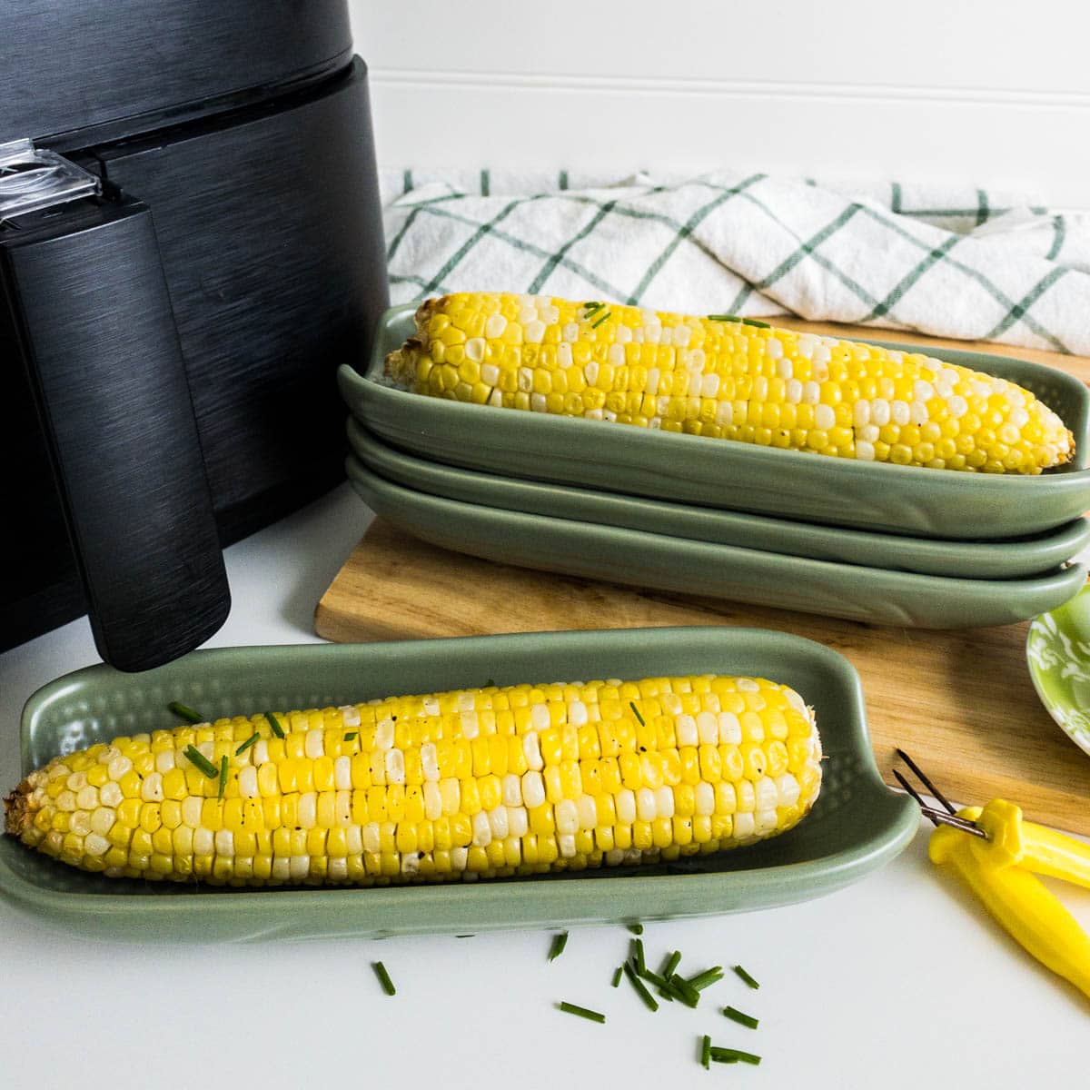 Corn on the cob in a green corn dish in front of an air fryer.