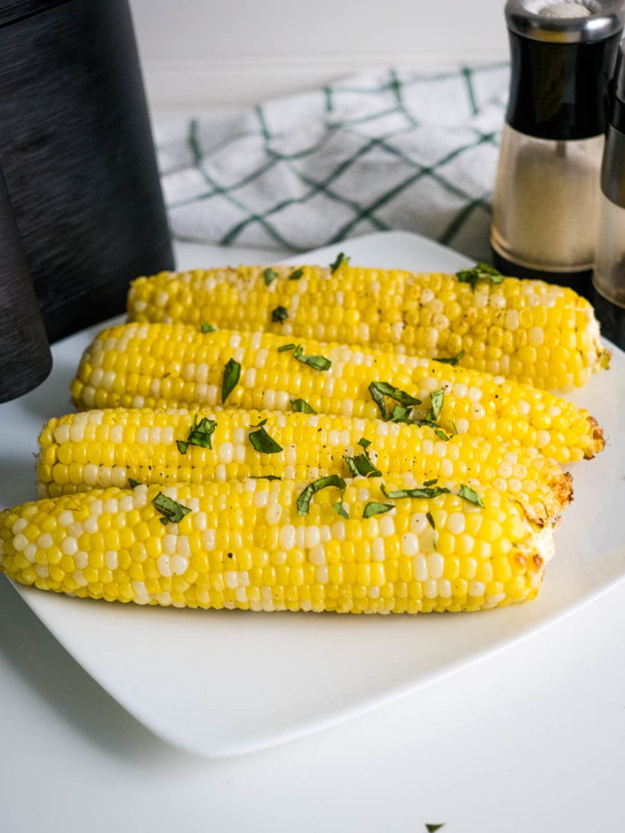 corn on a plate in front of air fryer with salt and pepper