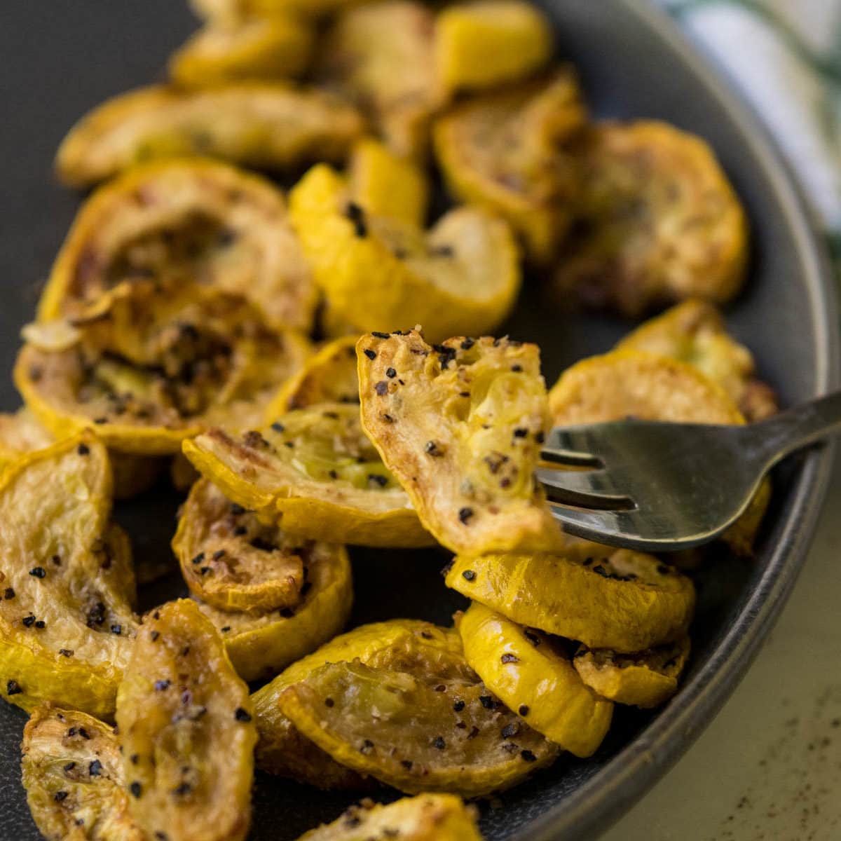 Air fryer yellow squash on a fork with more squash pieces in the background on a plate.