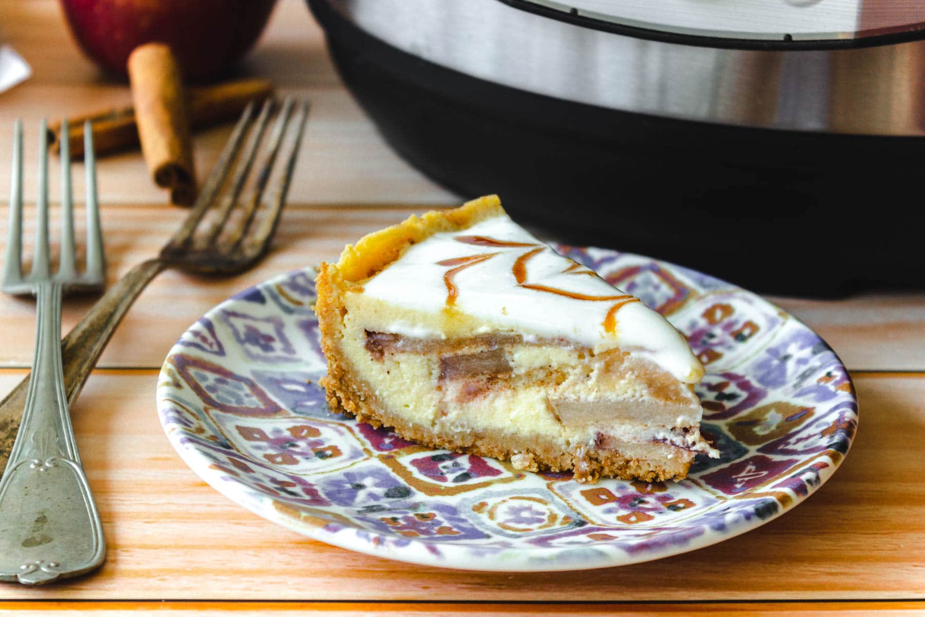 Slice of apple pie cheesecake in front of the Instant Pot.