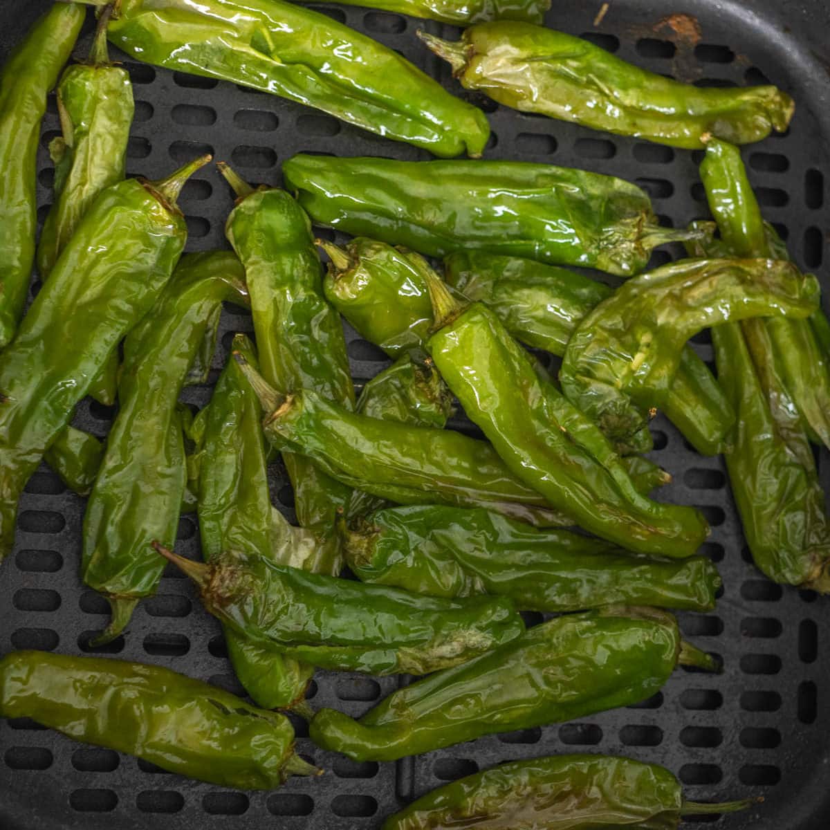 Plate of air fryer shishito peppers in front of air fryer.