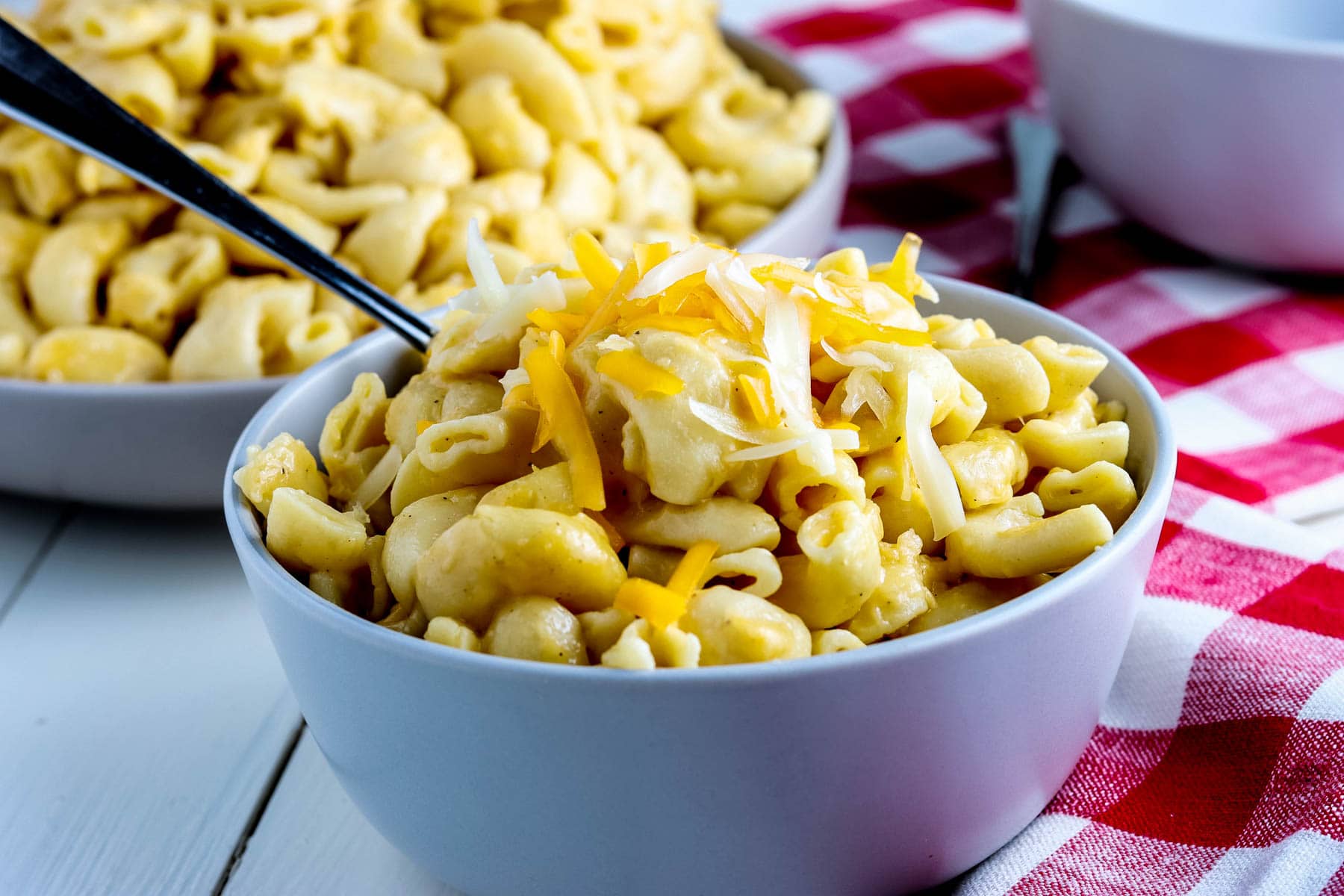 Two bowls of instant pot macaroni and cheese on a red and white checkered tablecloth.