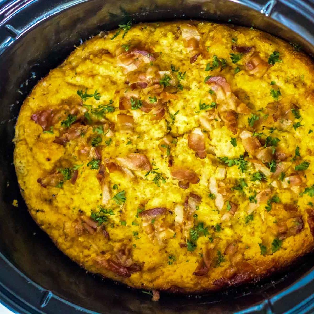 Top view of crock pot cornbread dressing with bacon and parsley on top.