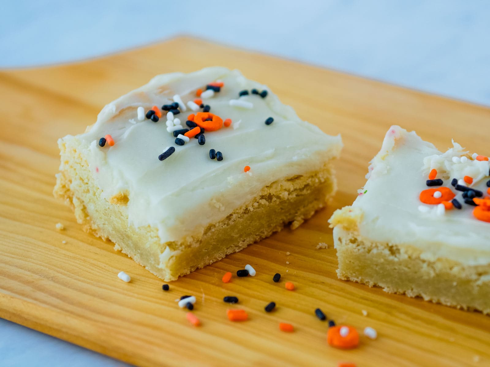 Two sugar cookie bars with sprinkles on a wooden cutting board.