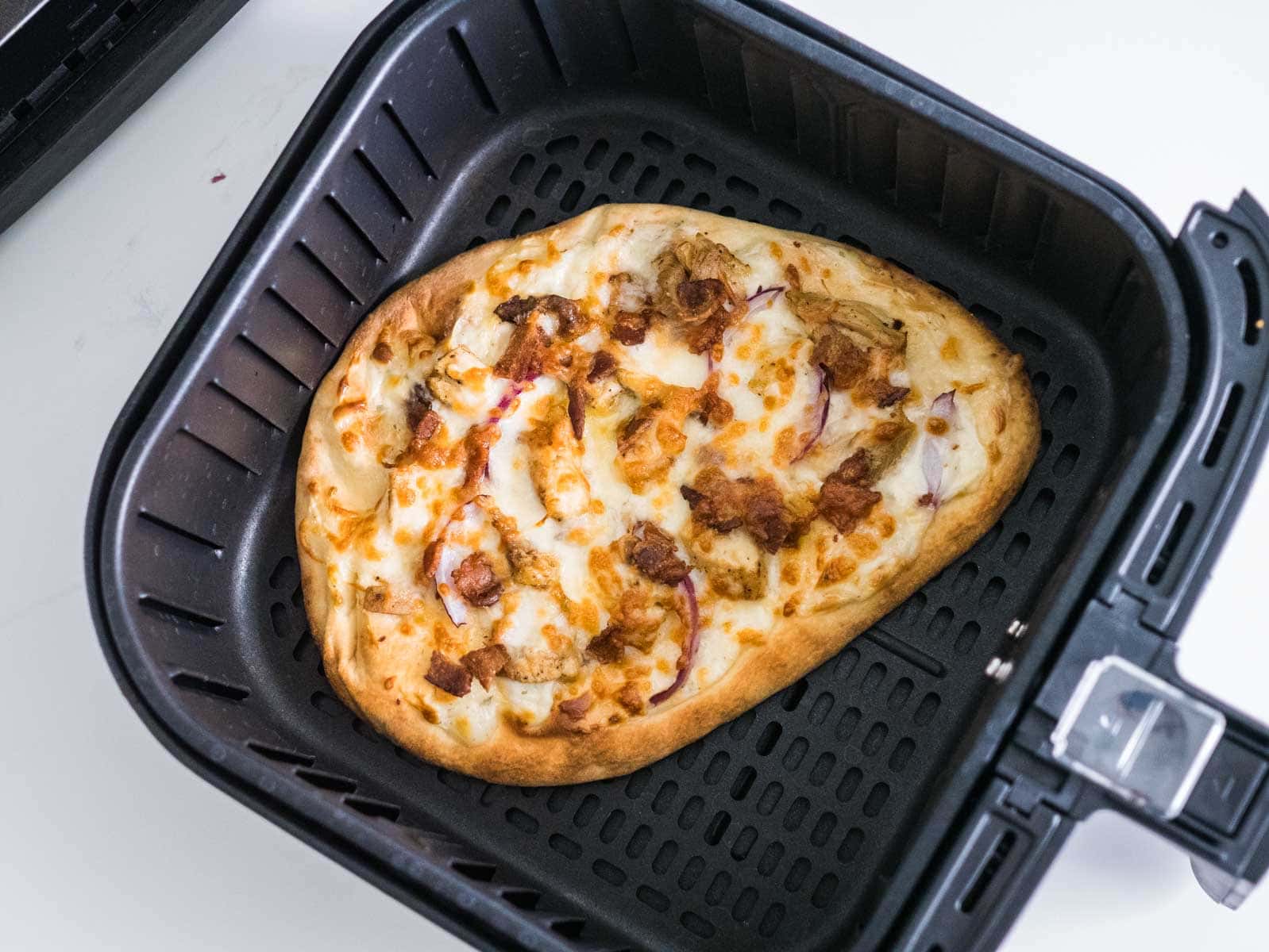 Naan pizza with chicken and bacon in the basket of an air fryer.