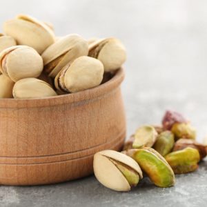 bowl of pistachios with some on the table in front of the bowl
