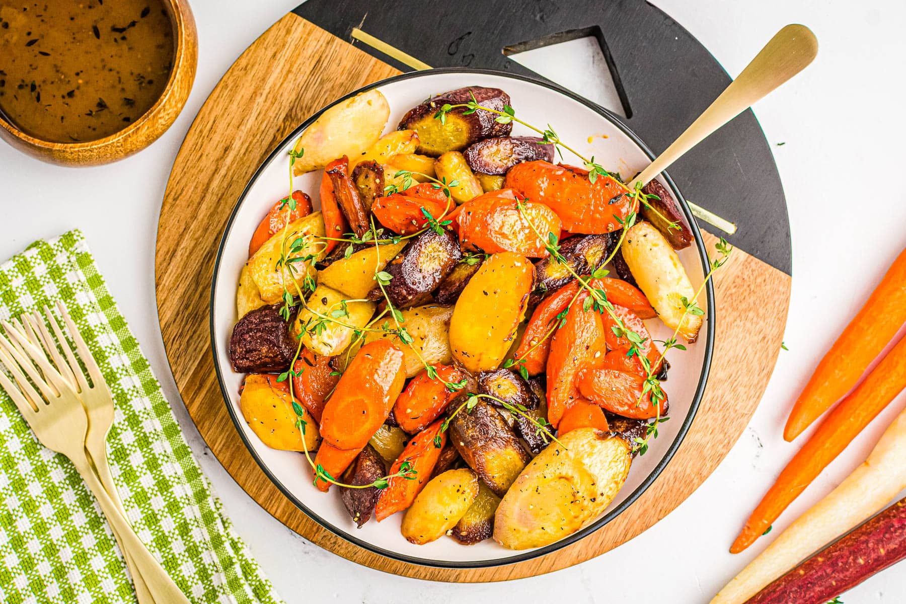 Multicolored carrots with a honey glaze one a plate with a green napkin at the side.