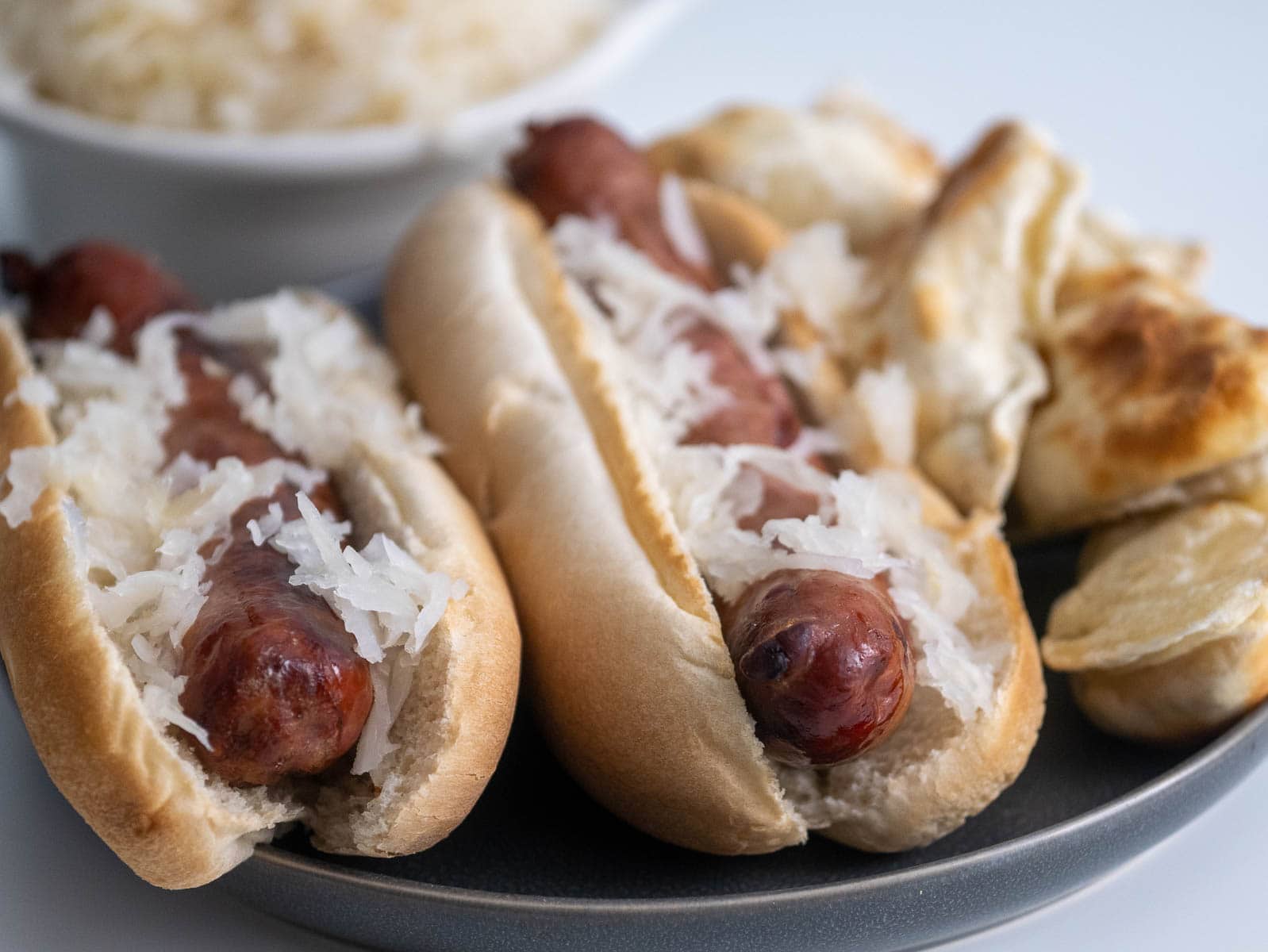 Two brats on a plate in buns topped with sauerkraut.