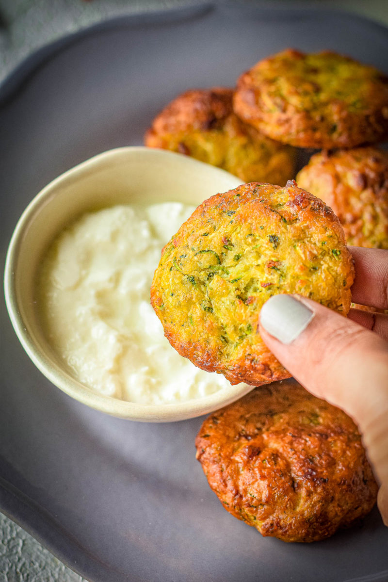 dipping a zucchini fritter in the sauce