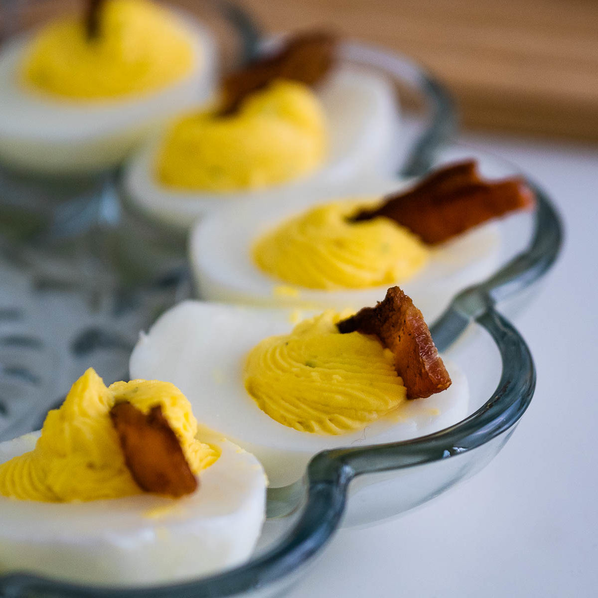 Deviled eggs with bacon in a glass deviled egg platter.