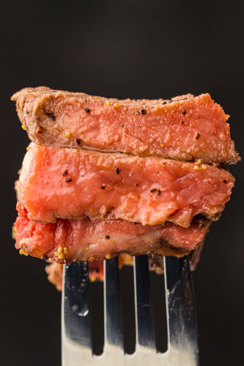 Close-up of air fryer steak slices speared on a fork, showing pink interior and seasoned crust against a dark background.