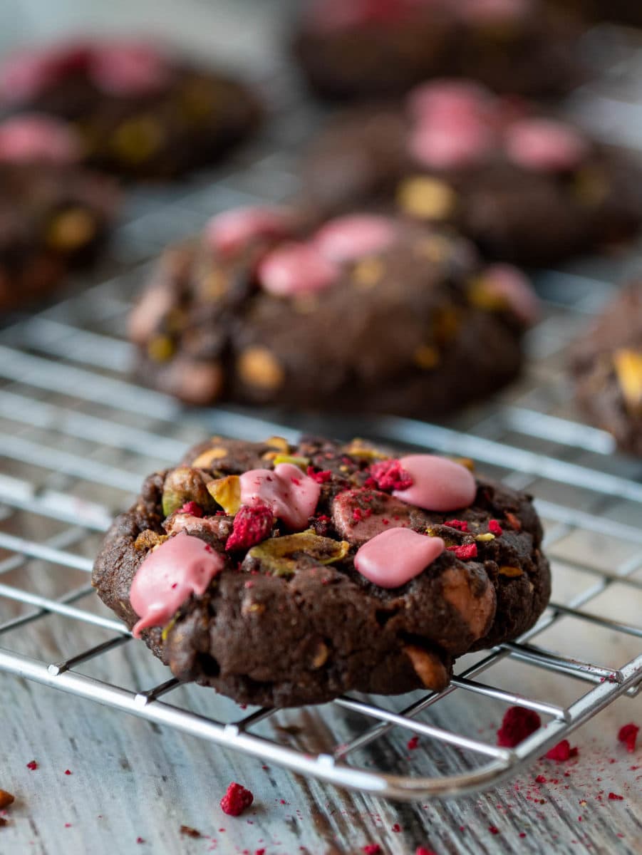 ruby chocolate chip cookie with pistachios and freeze dried raspberries on a cooling rack