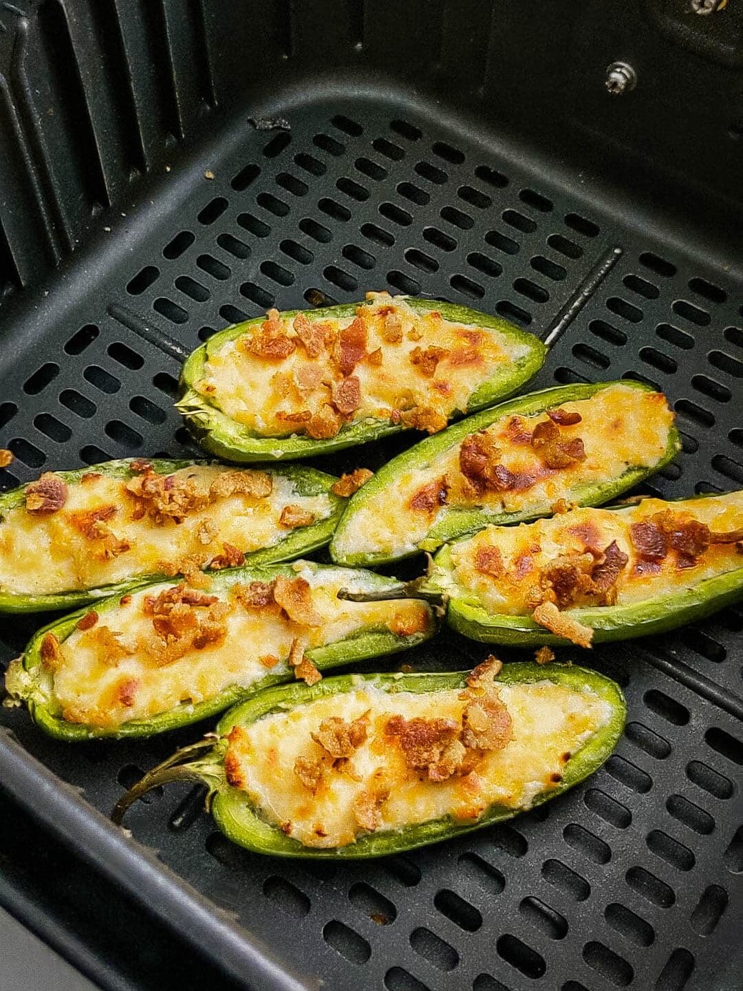 Cooked jalapeno poppers in air fryer basket.