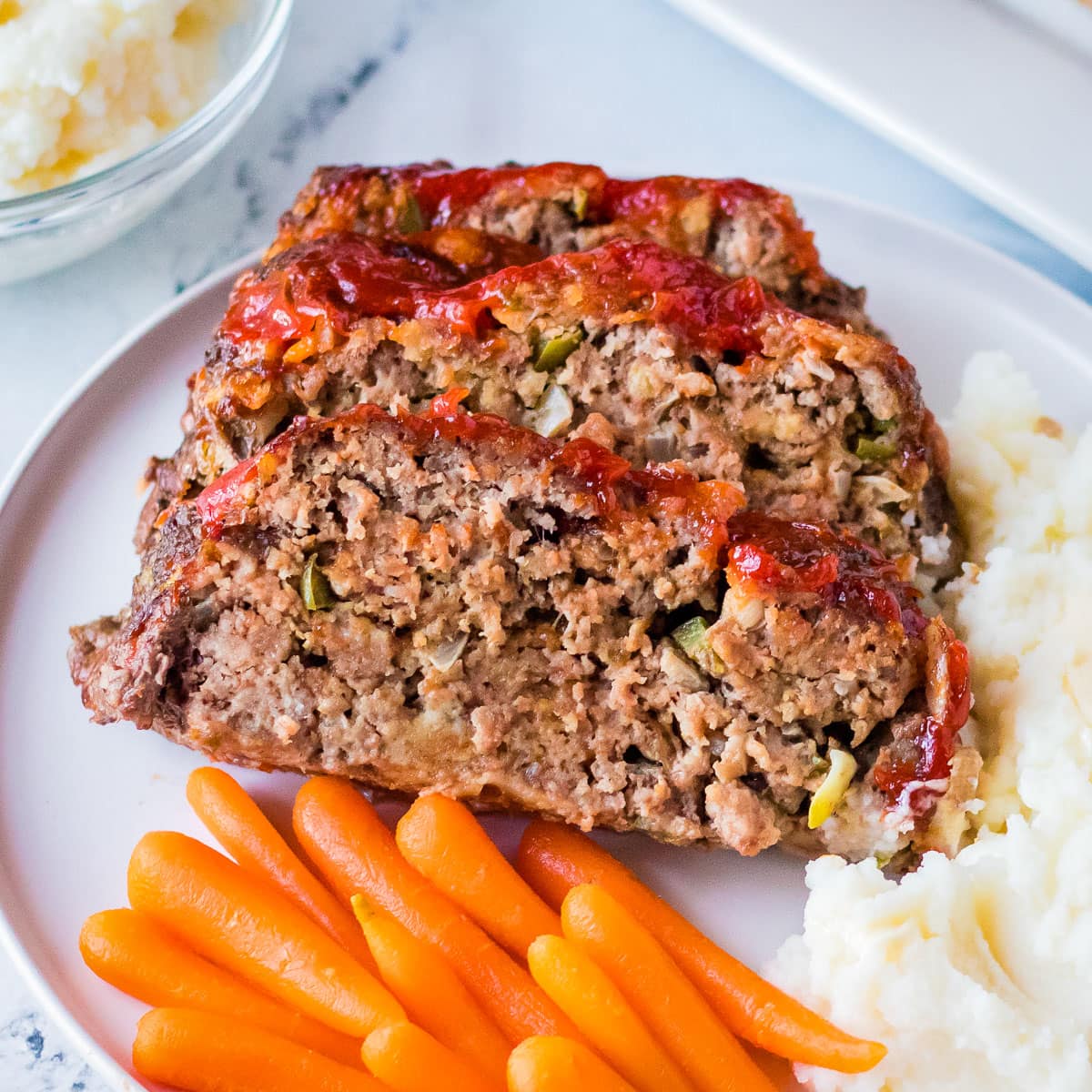 Two slices of meatloaf on a plate with mashed potatoes and carrots.