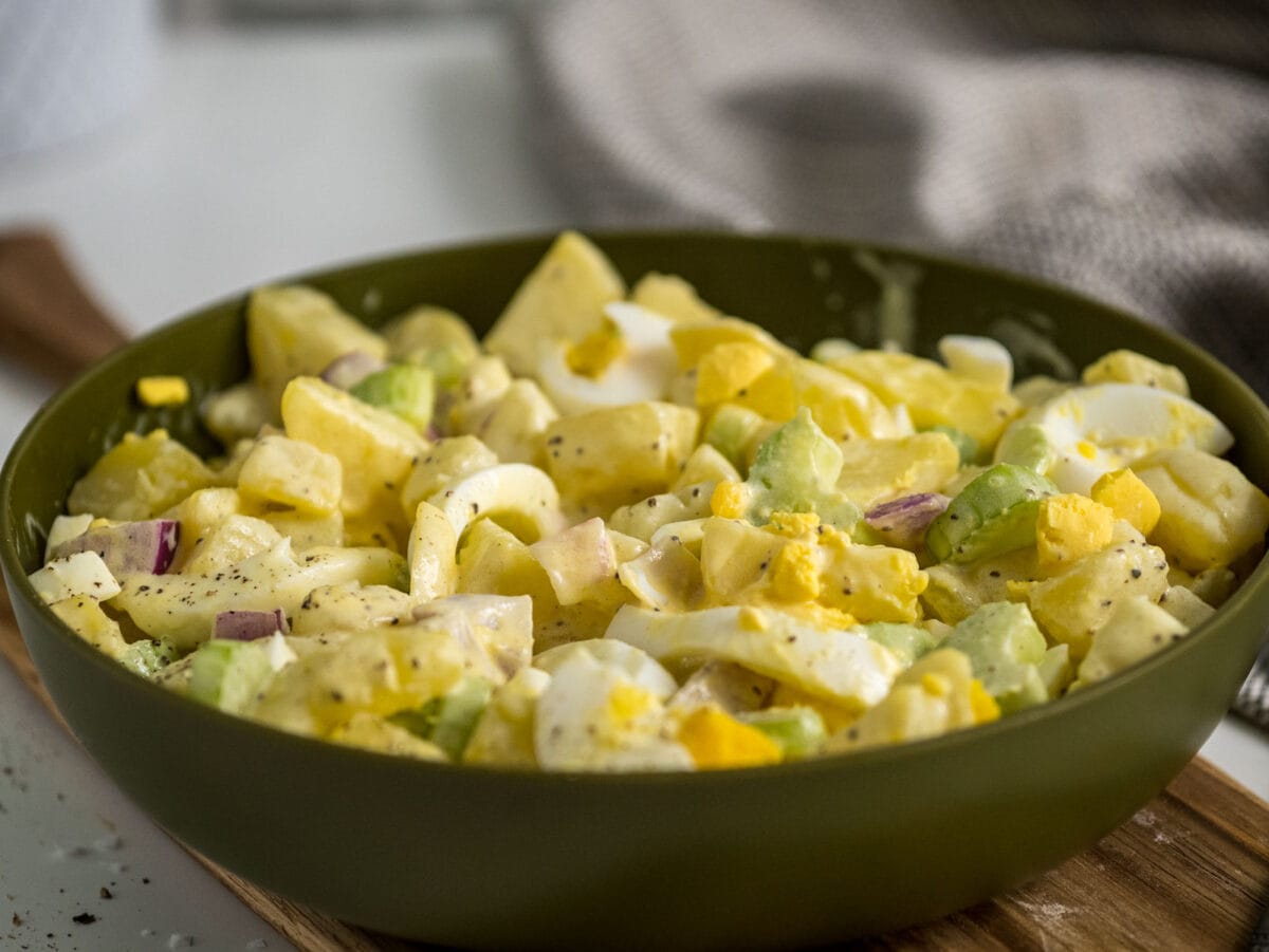 side view of creamy potato salad in a bowl on a cutting board.
