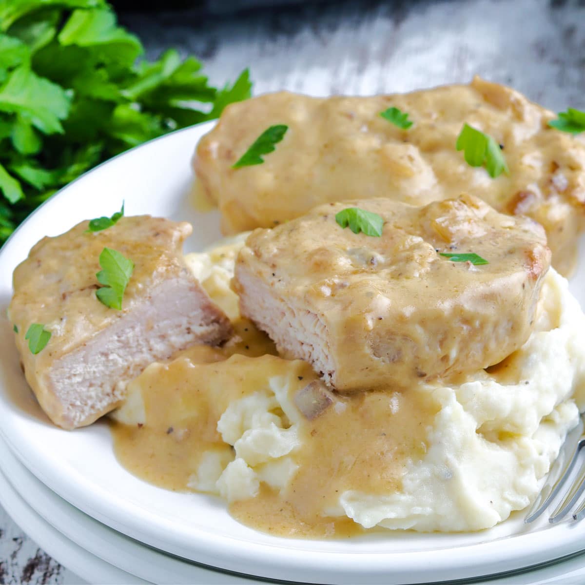 Slow Cooker Pork Chops on a plate covered with a creamy mushroom gravy and served on mashed potatoes.