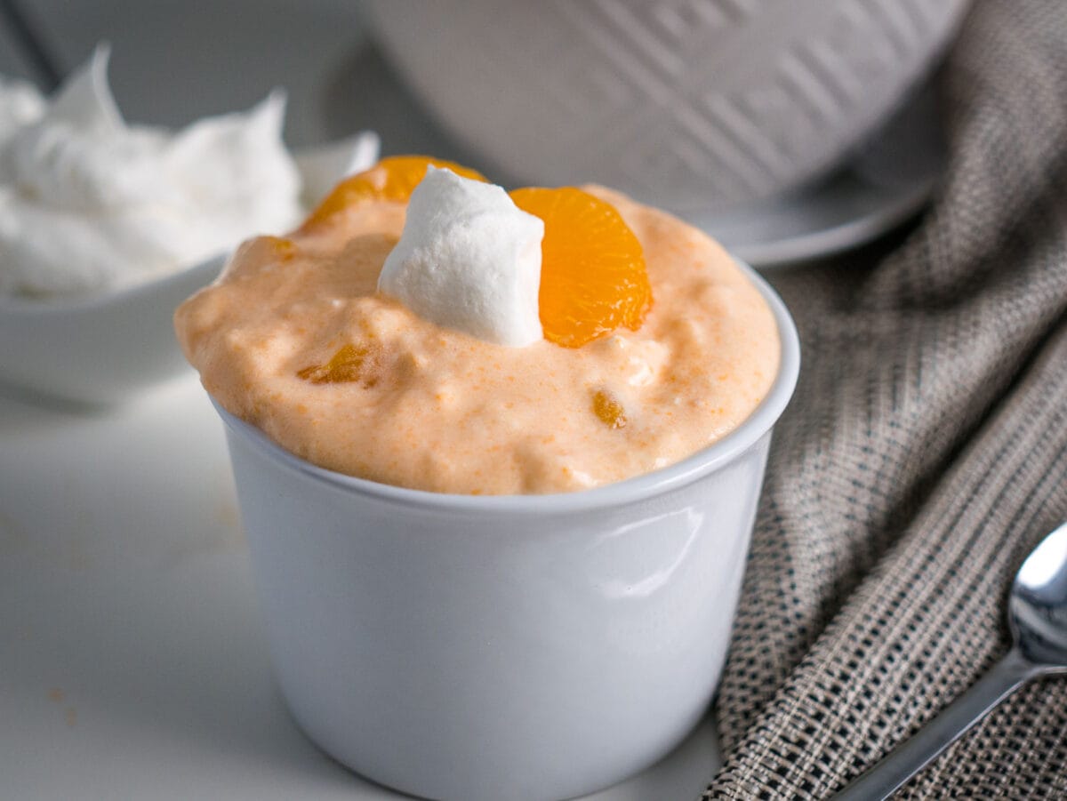orange fluff salad in a bowl with whipped cream.