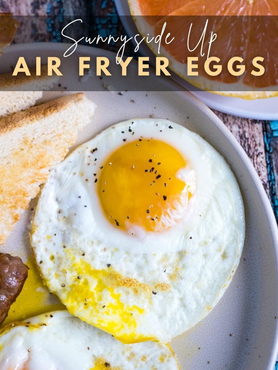 Plate with sunny-side up egg seasoned with pepper, served with toast and sausage. Text overlay reads: "Sunnyside Up Air Fryer Eggs—perfectly cooked fried eggs in air fryer for a quick and tasty breakfast.
