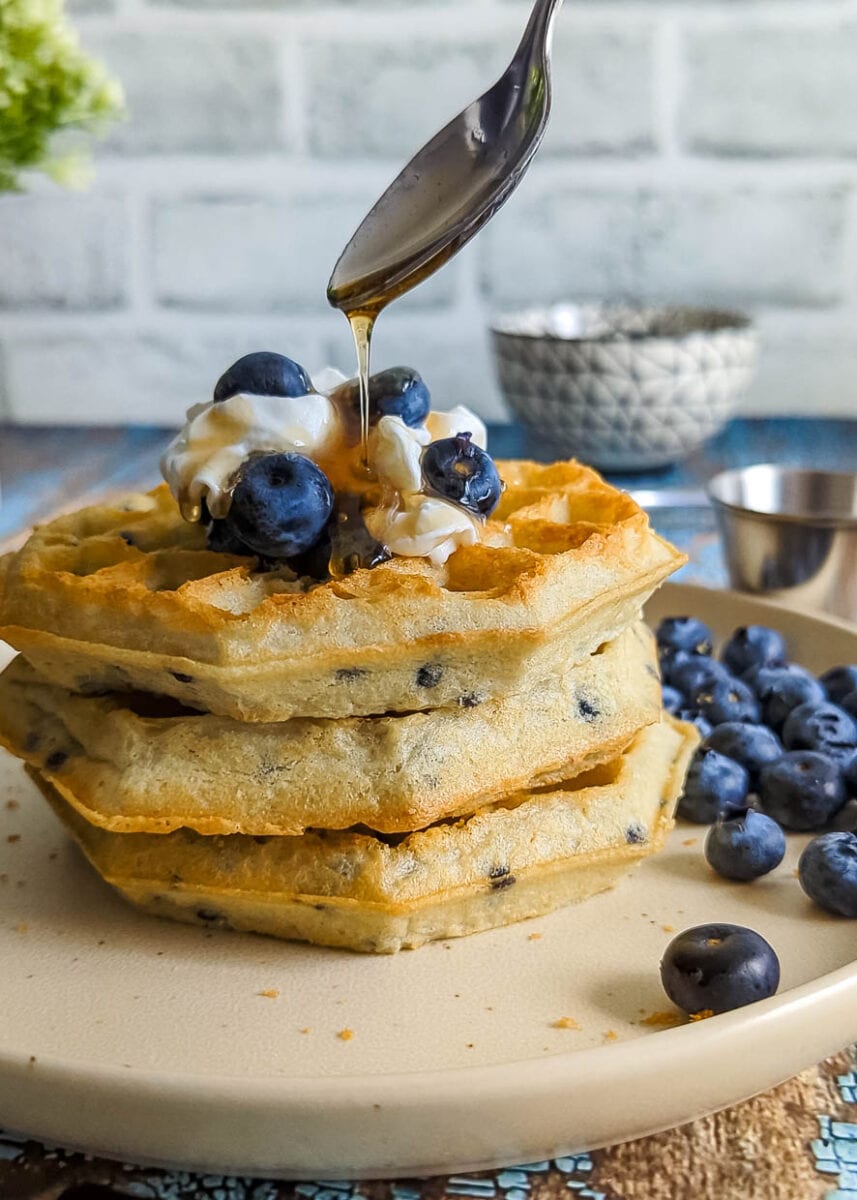 drizzling blueberry air fryer waffles with syrup.