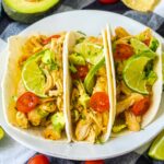 three chicken tacos on a plate with toppings.