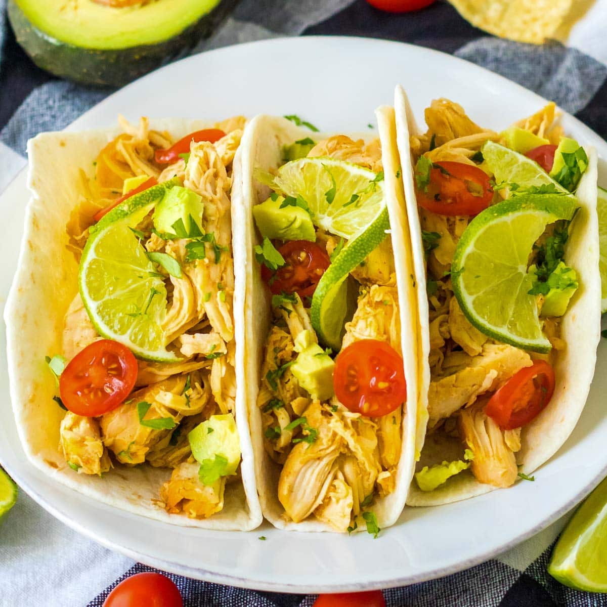 Three slow cooker tacos with chicken, lime, avocado and tomatoes.
