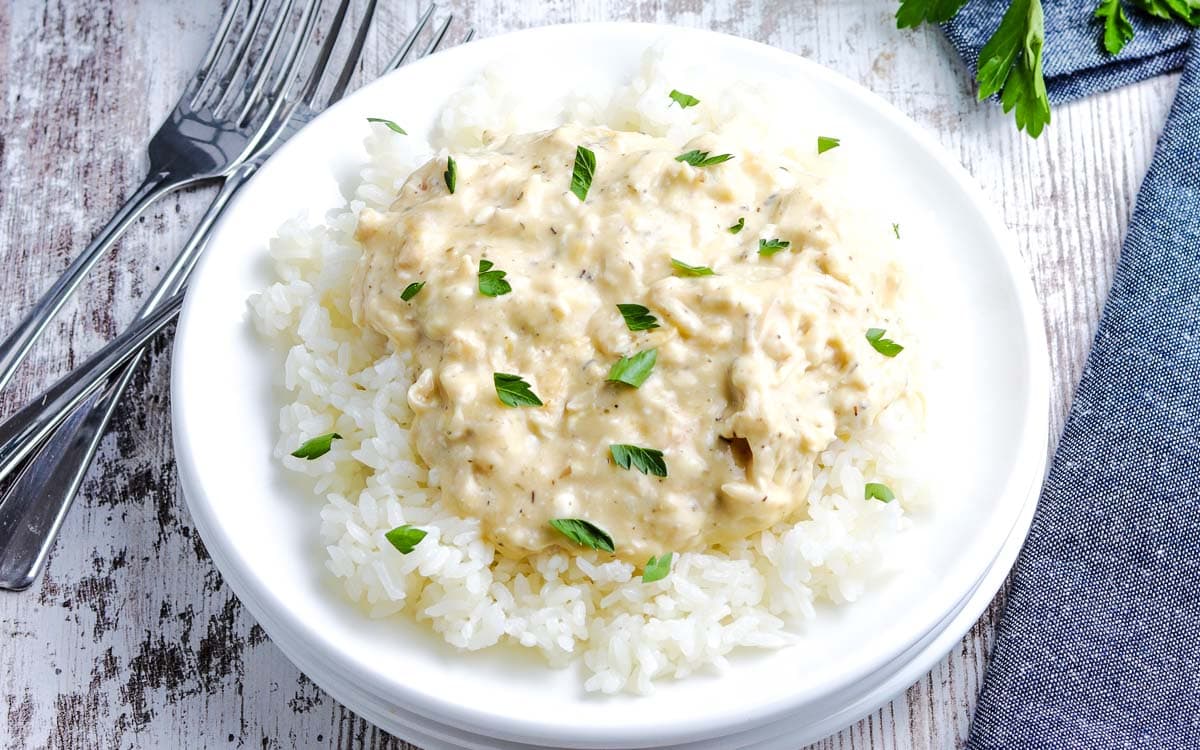 Slow Cooker Creamy Chicken on a white plate on rice topped with parsley.