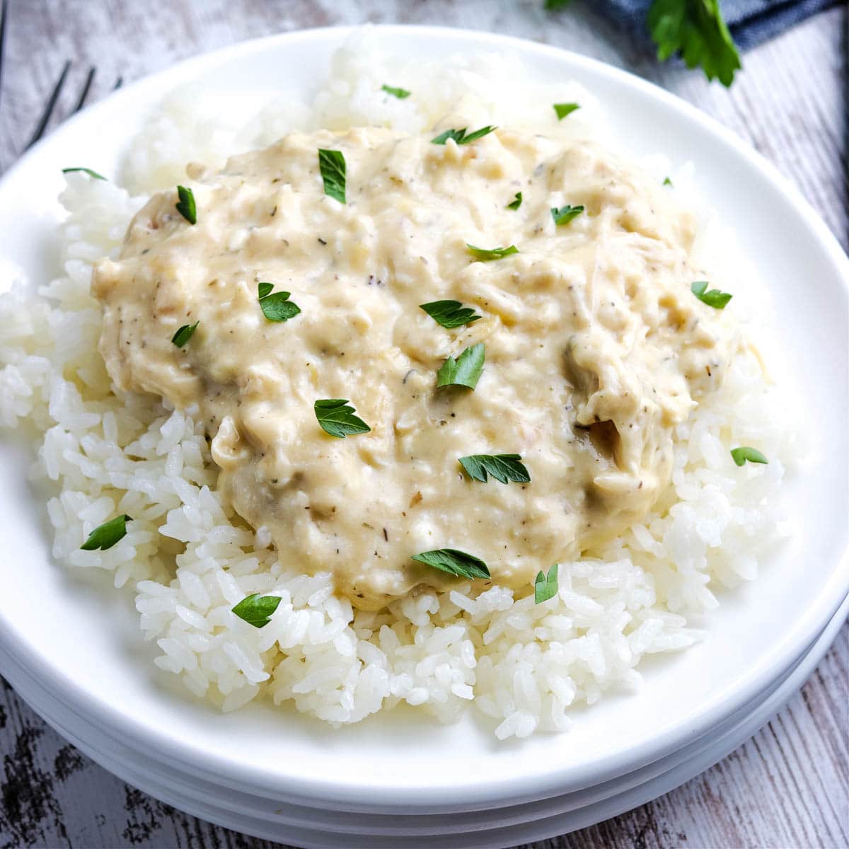 Slow Cooker Creamy Chicken on a white plate on rice topped with parsley.