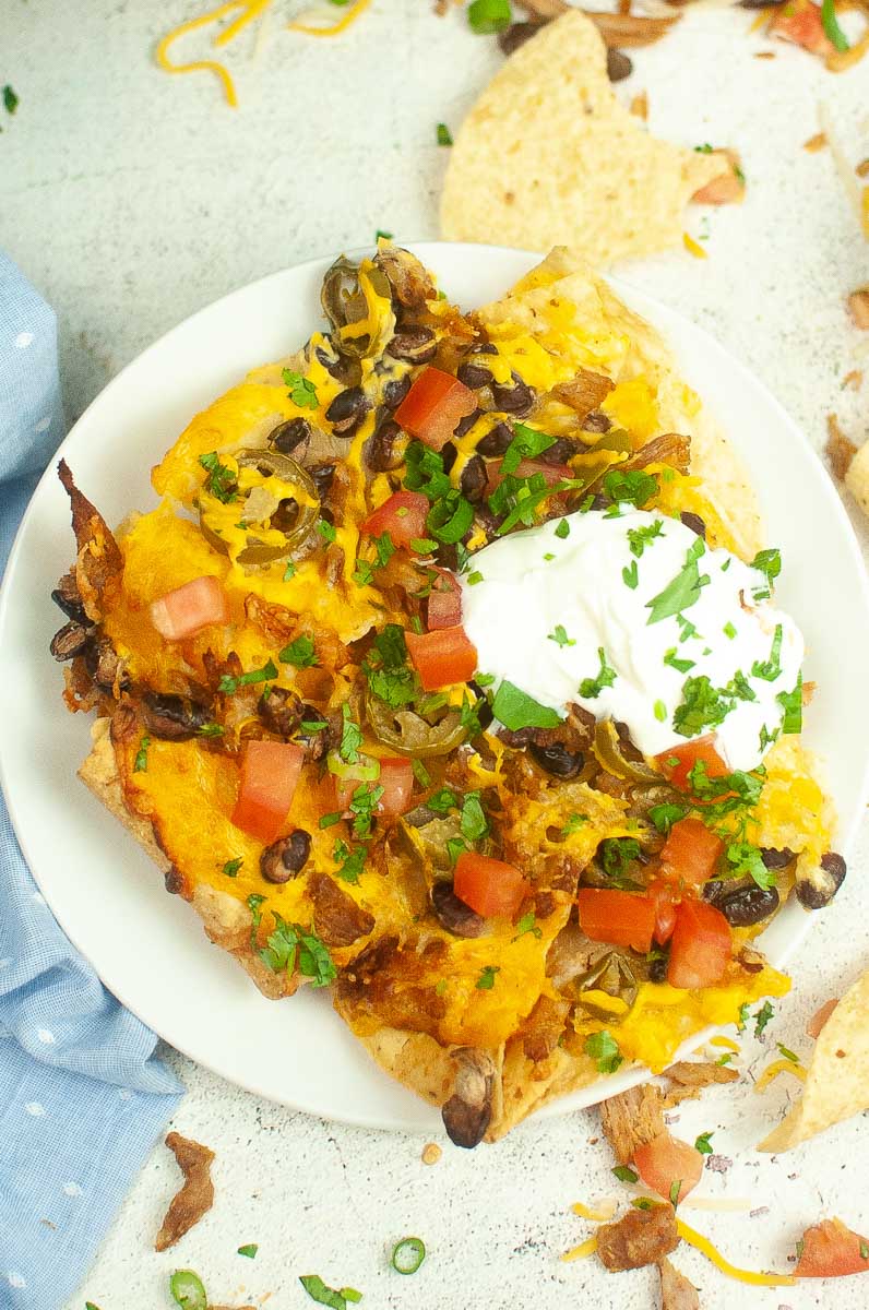top view of air fryer nachos with cheese, tomatoes, green onions and sour cream.