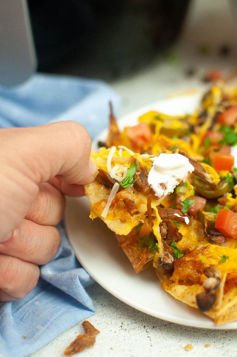 holding a tortilla chip loaded with nacho toppings.