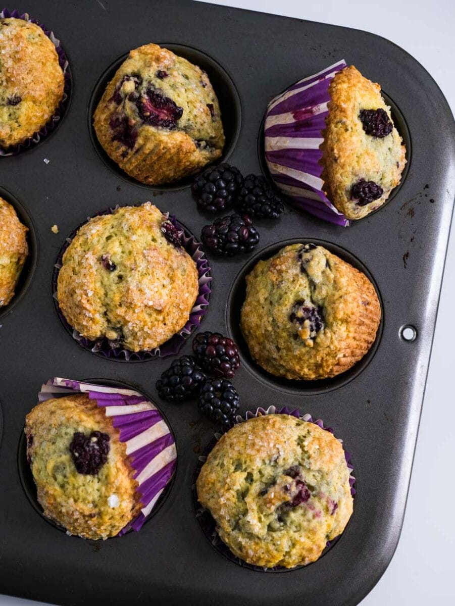 top view of blackberry muffins in a muffin tin tilted to show the sides and top with blackberries.