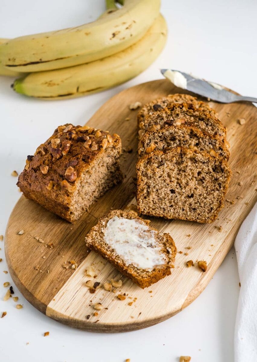 slices of banana bread on a wooden cutting board one of which is buttered.