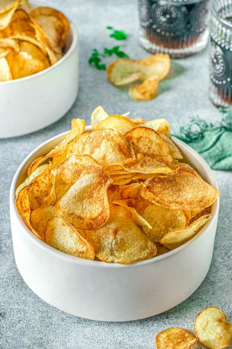 Air fryer potato chips with more chips in the background and a glass of soda.