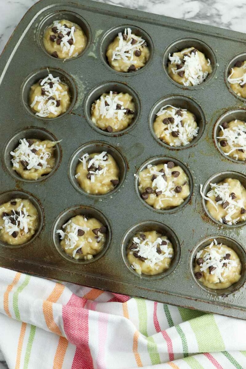 Muffin batter in tins topped with chocolate and coconut.
