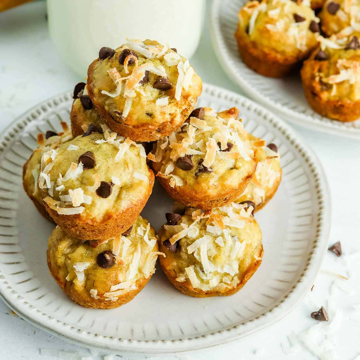 Stack of banana coconut muffins on a white plate with chocolate chips scattered around.