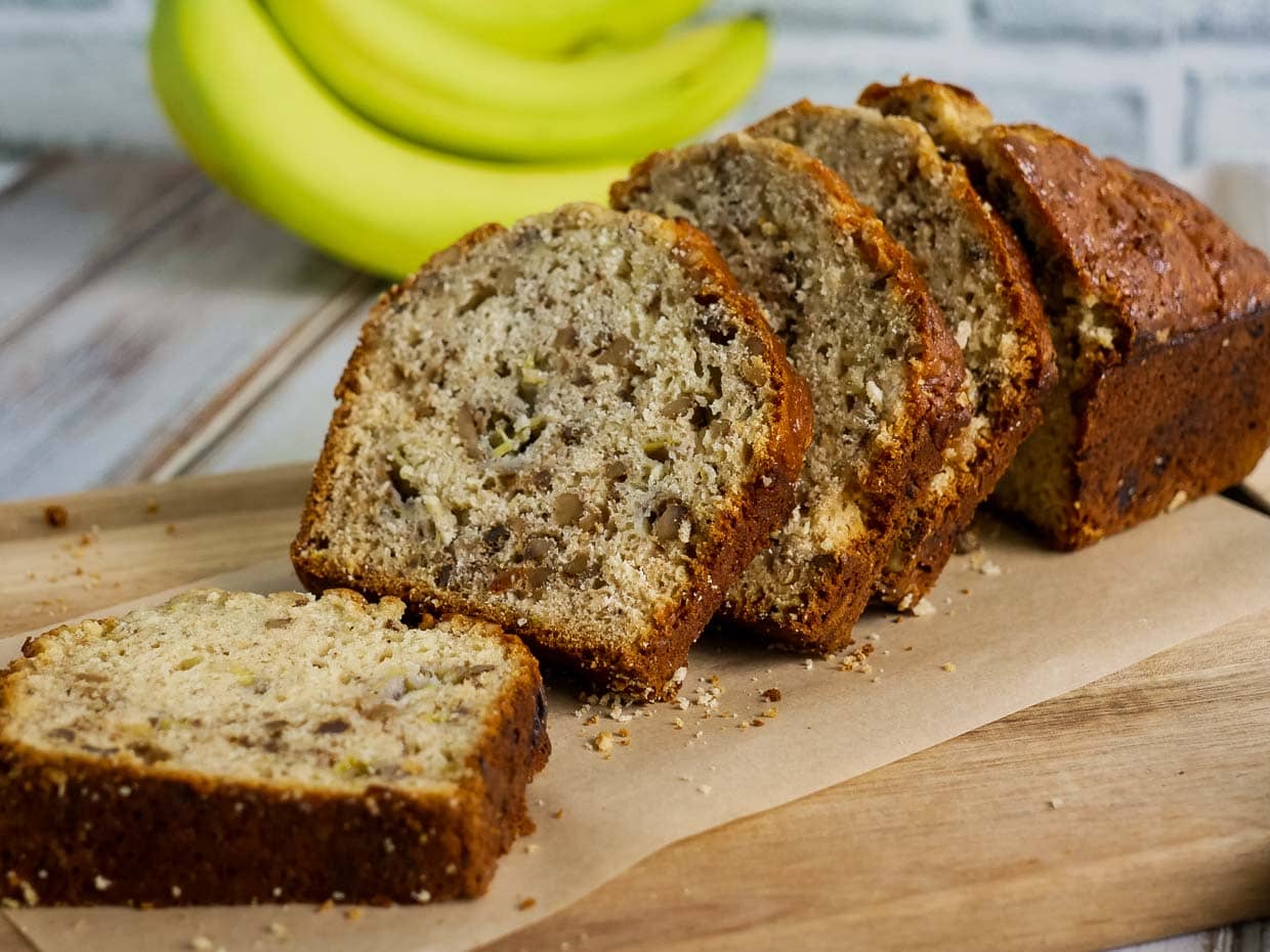Sliced loaf of Bisquick banana bread on a cutting board with bananas in the background.