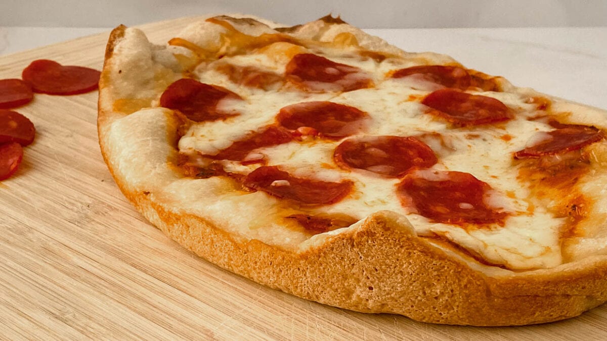 side view of pepperoni pizza on a cutting board.