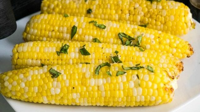 air fryer corn on the cob on a plate with basil.