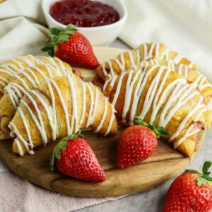 Jam crescent rolls on a wooden cutting board with strawberries around.