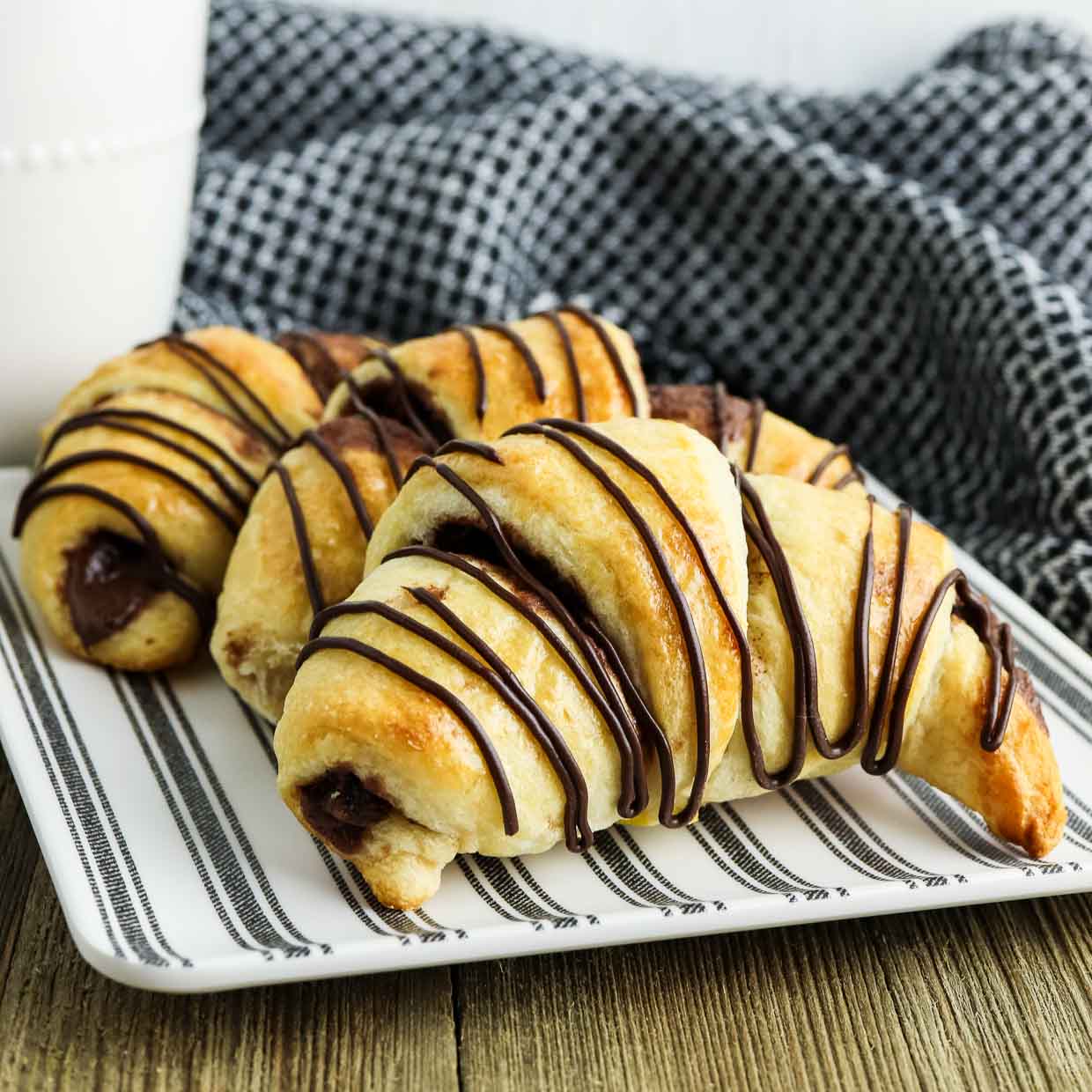 Three nutella crescent rolls on a plate drizzled with chocolate.