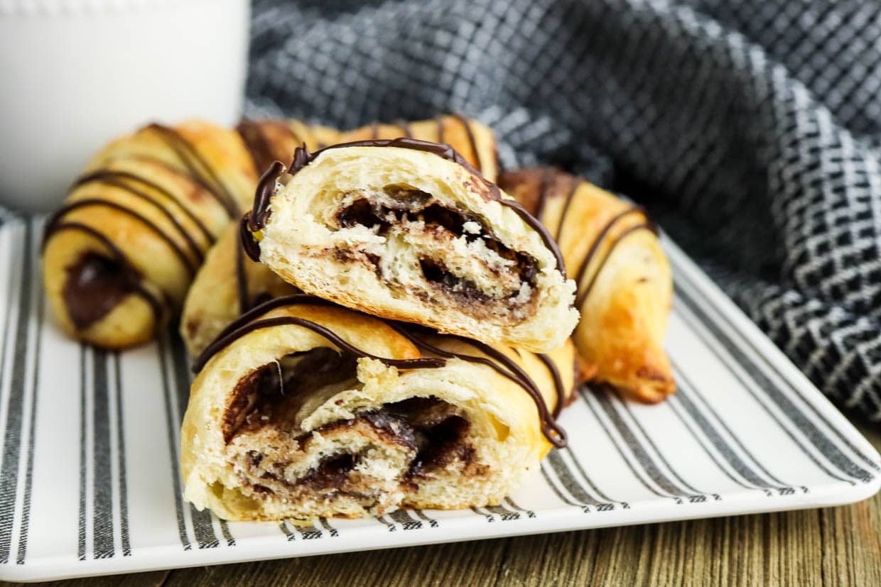 Three nutella crescent rolls on a plate drizzled with chocolate.