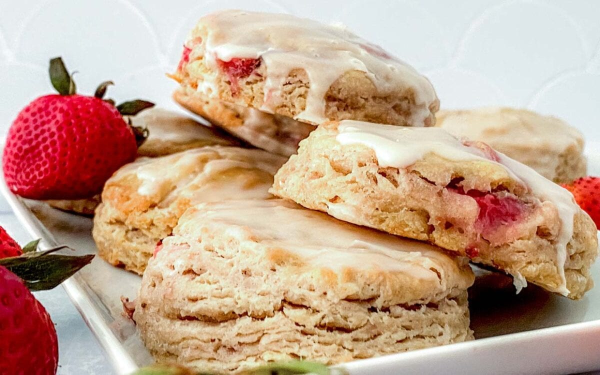 Strawberry biscuits piled up on a white plate with strawberries around.