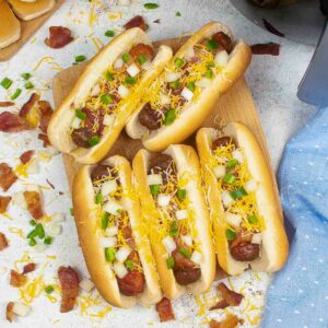 Top view of air fryer bacon wrapped hot dogs with jalapenos, onions and cheese.