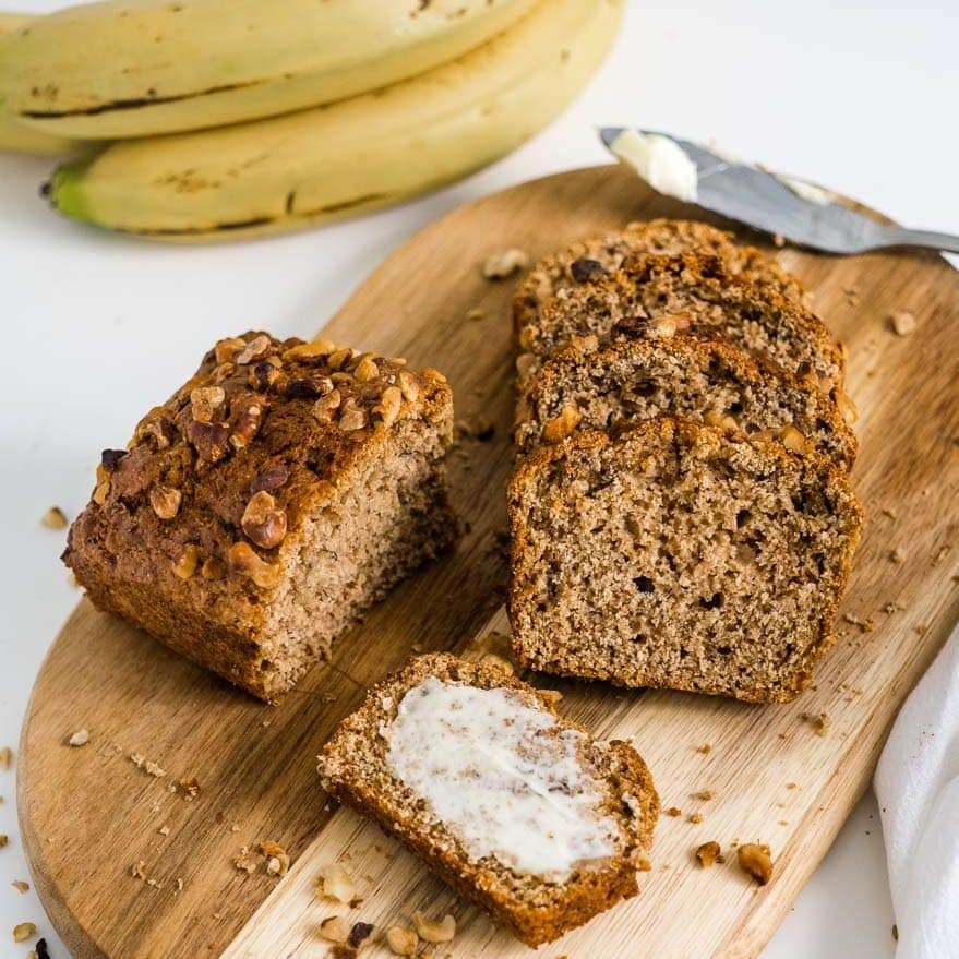 slices of banana bread on a wooden cutting board one of which is buttered.
