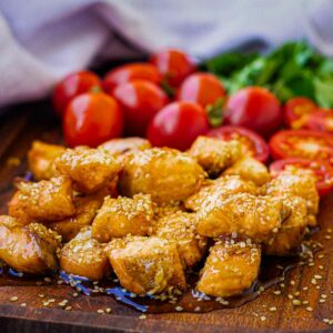 Closeup of air fryer salmon bites on a cutting board with tomtatoes.