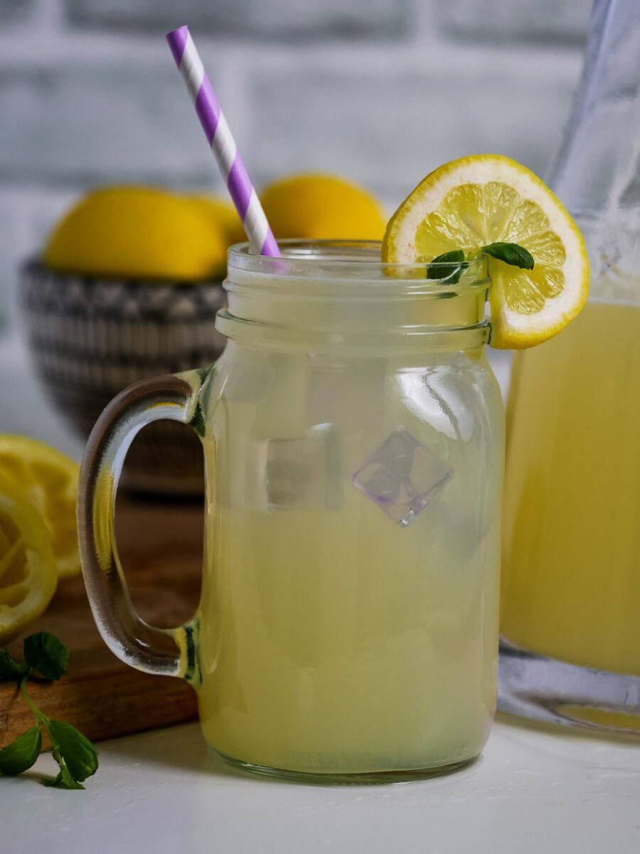 Glass of lemonade on a table with lemons in the background.