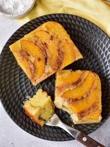 Top view of two pieces of peach upside down cake on a black plate.