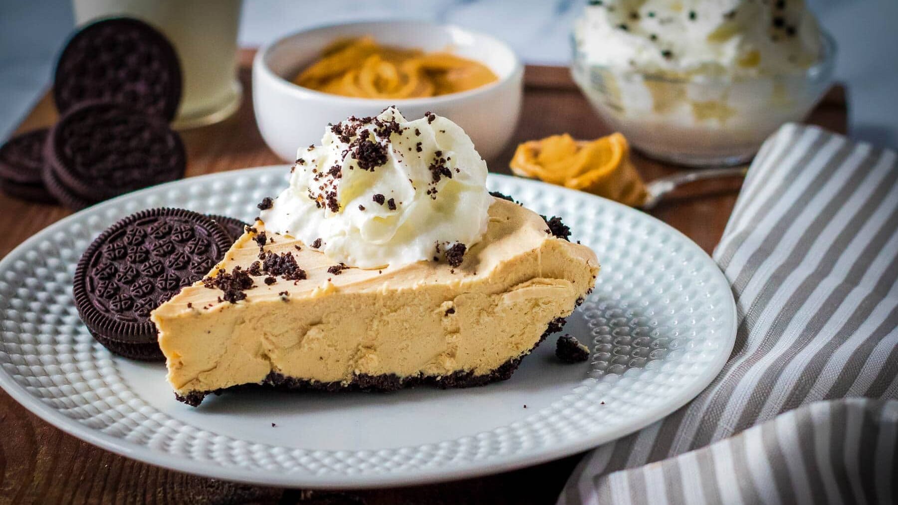 Side view of a slice of peanut butter pie topped with whipped cream on a plate.